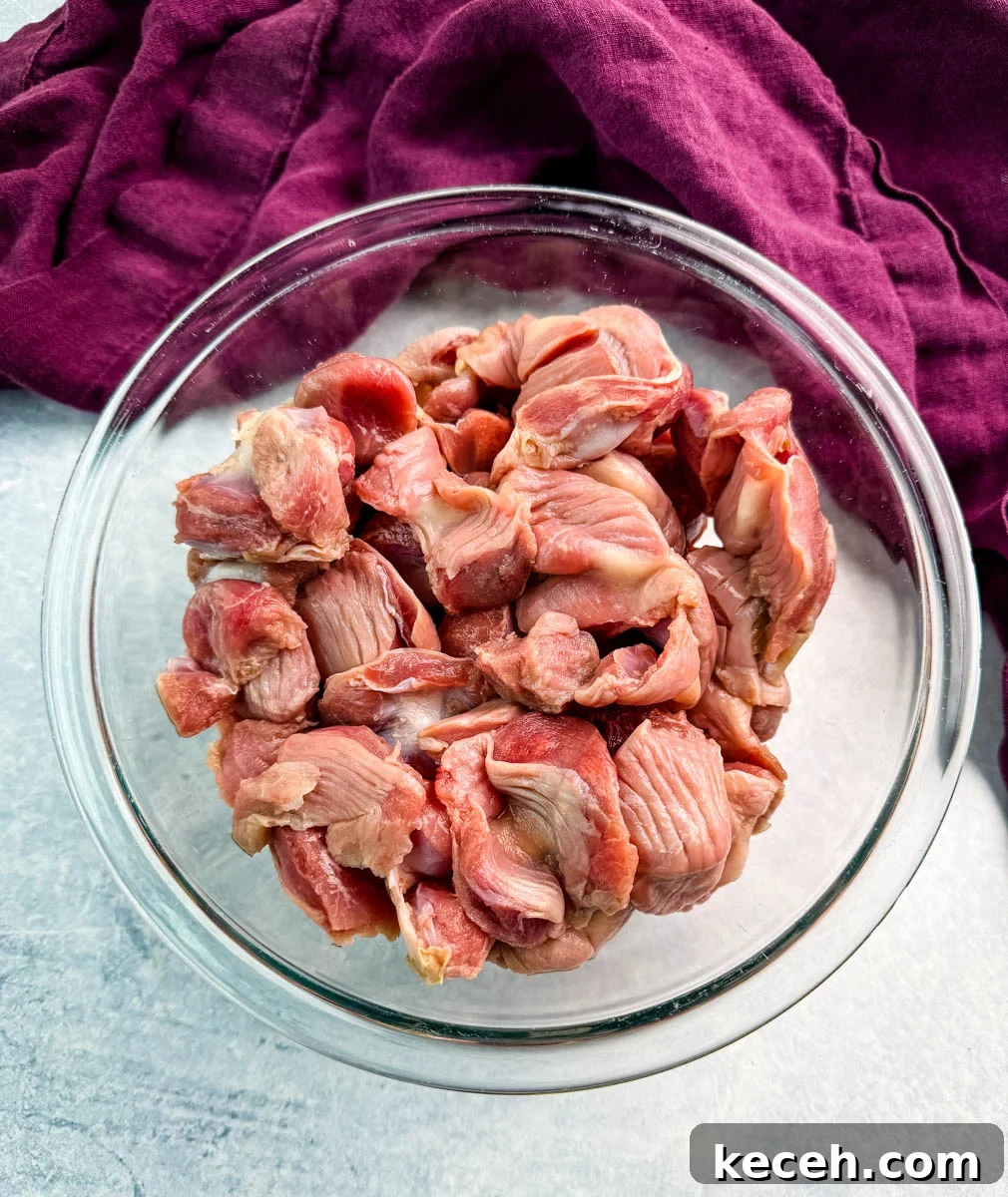 Crispy Fried Chicken Gizzards Recipe: Southern-Style Crunch 5 Overhead view of raw chicken gizzards in a clear glass bowl, set on a light background with a purple cloth nearby.