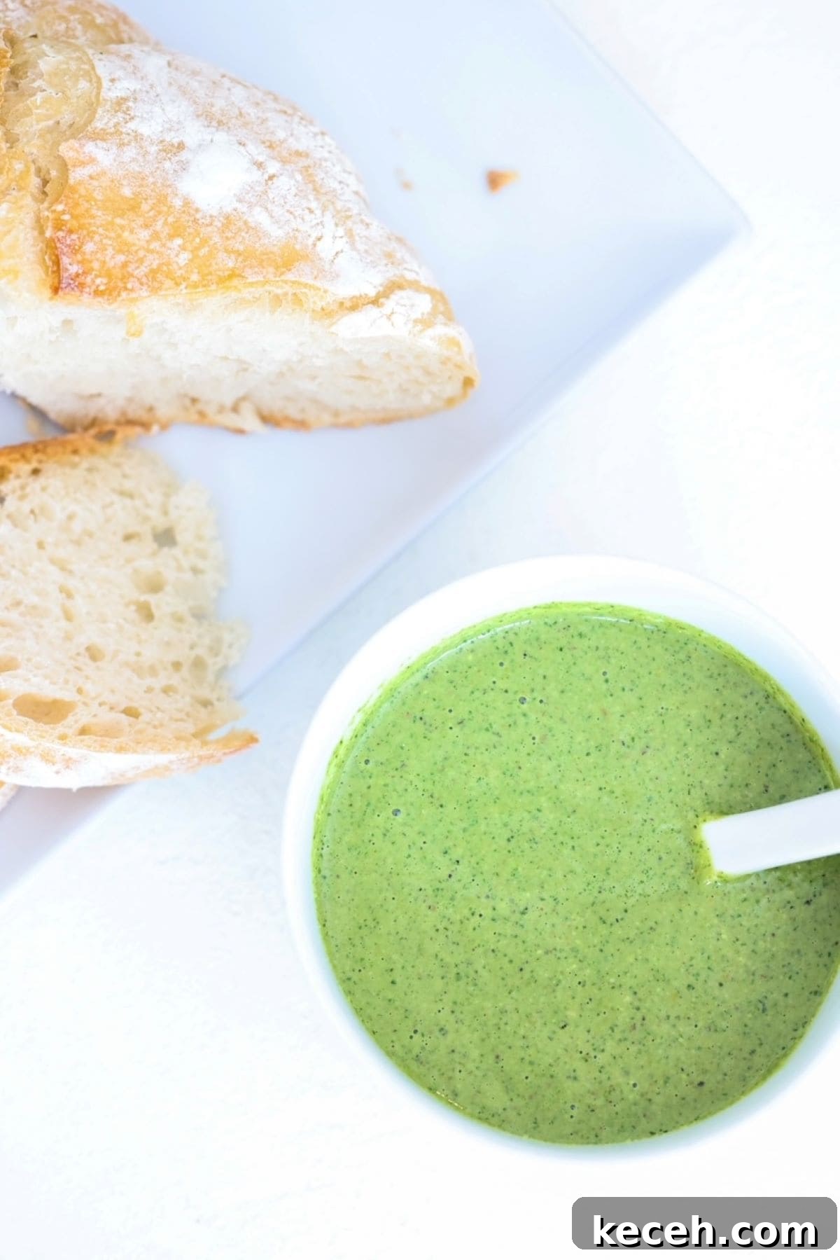 Pesto in a white bowl and two slices of sourdough bread on a white plate.