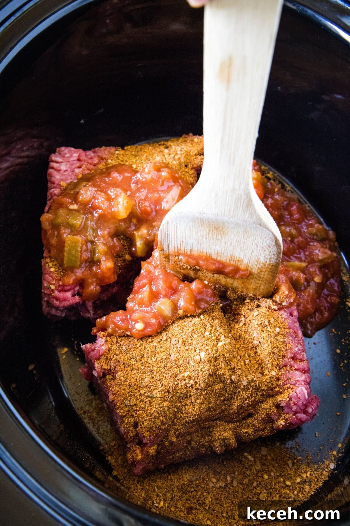 A spatula is used to break up the ground beef inside the slow cooker.