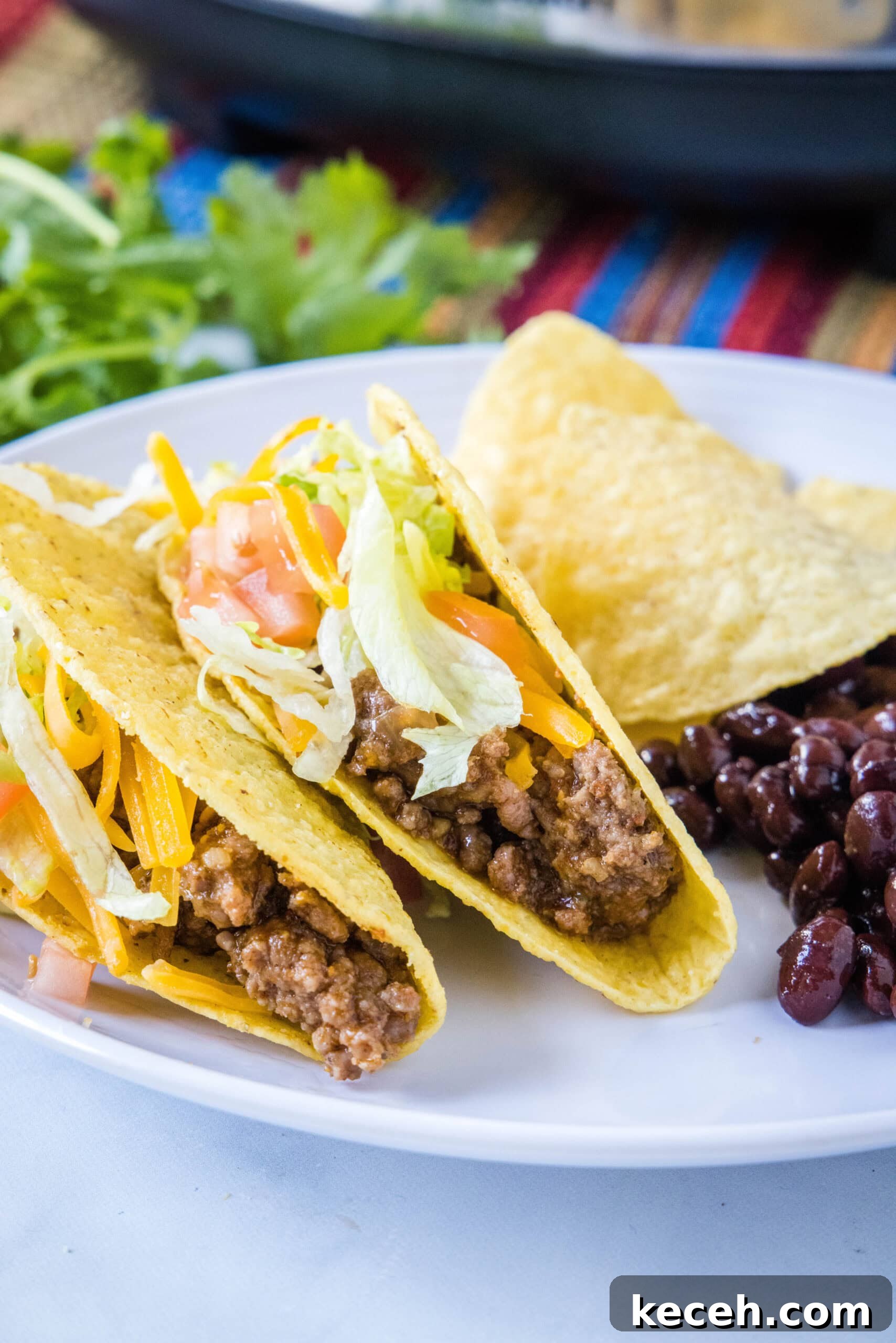 Tacos filled with ground beef on a white plate next to black beans.