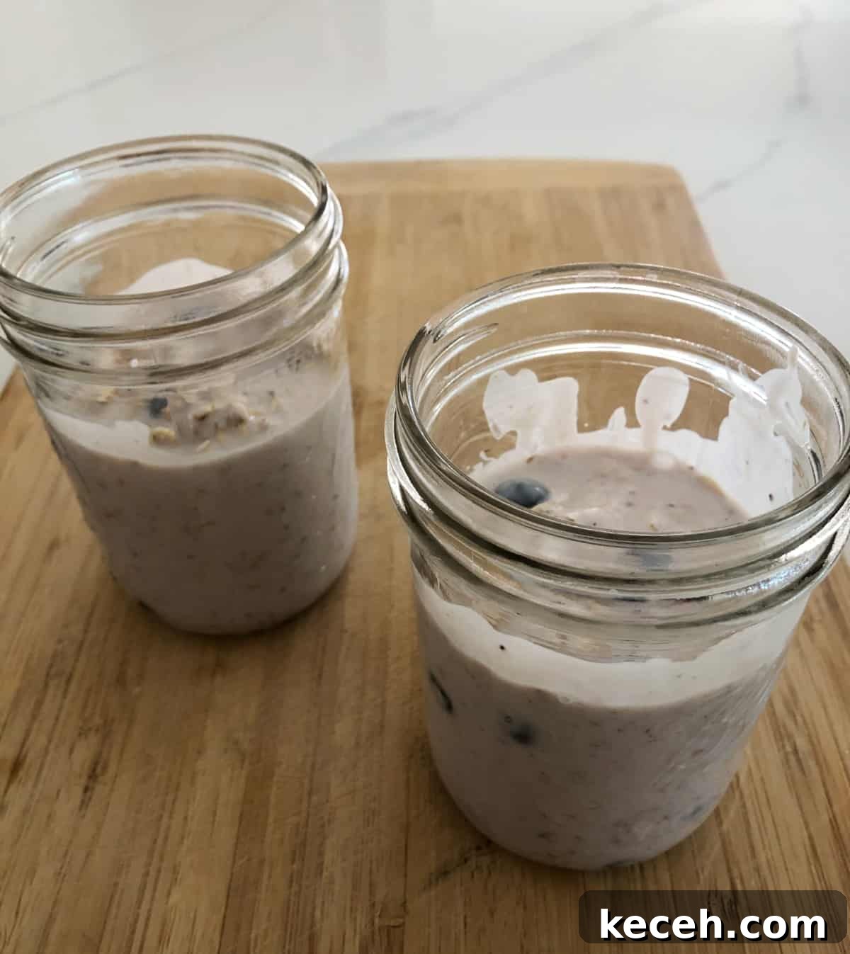 Blueberry and Maple Overnight Oats Recipe for Quick Breakfast 6 Two mason jars with overnight oats on bamboo cutting board.