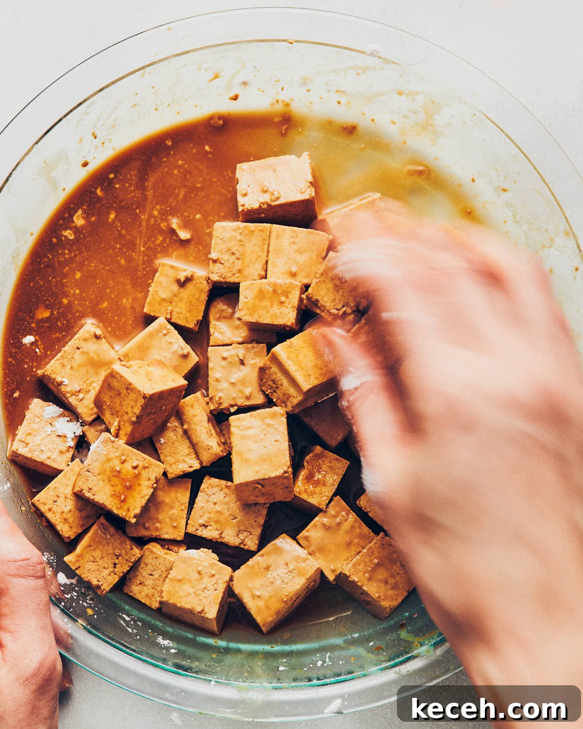 Crispy Air Fryer Breaded Tofu Recipe 11 A woman's hands tossing cubes of tofu with tamari and cornstarch, until the cornstarch is no longer visible