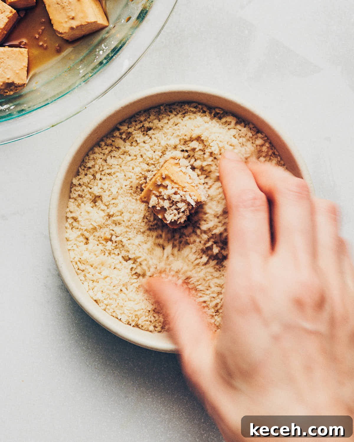 Crispy Air Fryer Breaded Tofu Recipe 12 A hand putting tofu into a dish of panko breadcrumbs to create a crust