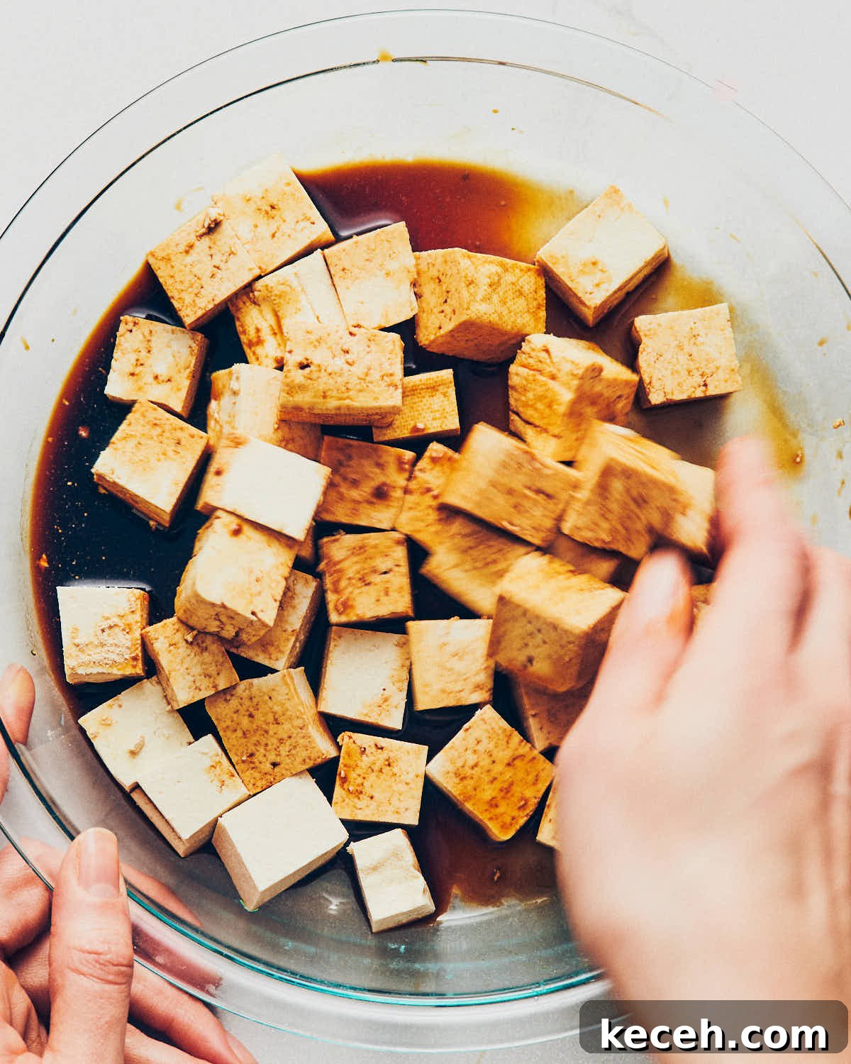 Crispy Air Fryer Breaded Tofu Recipe 7 A hand tossing cubed tofu and tamari until the tofu is well coated