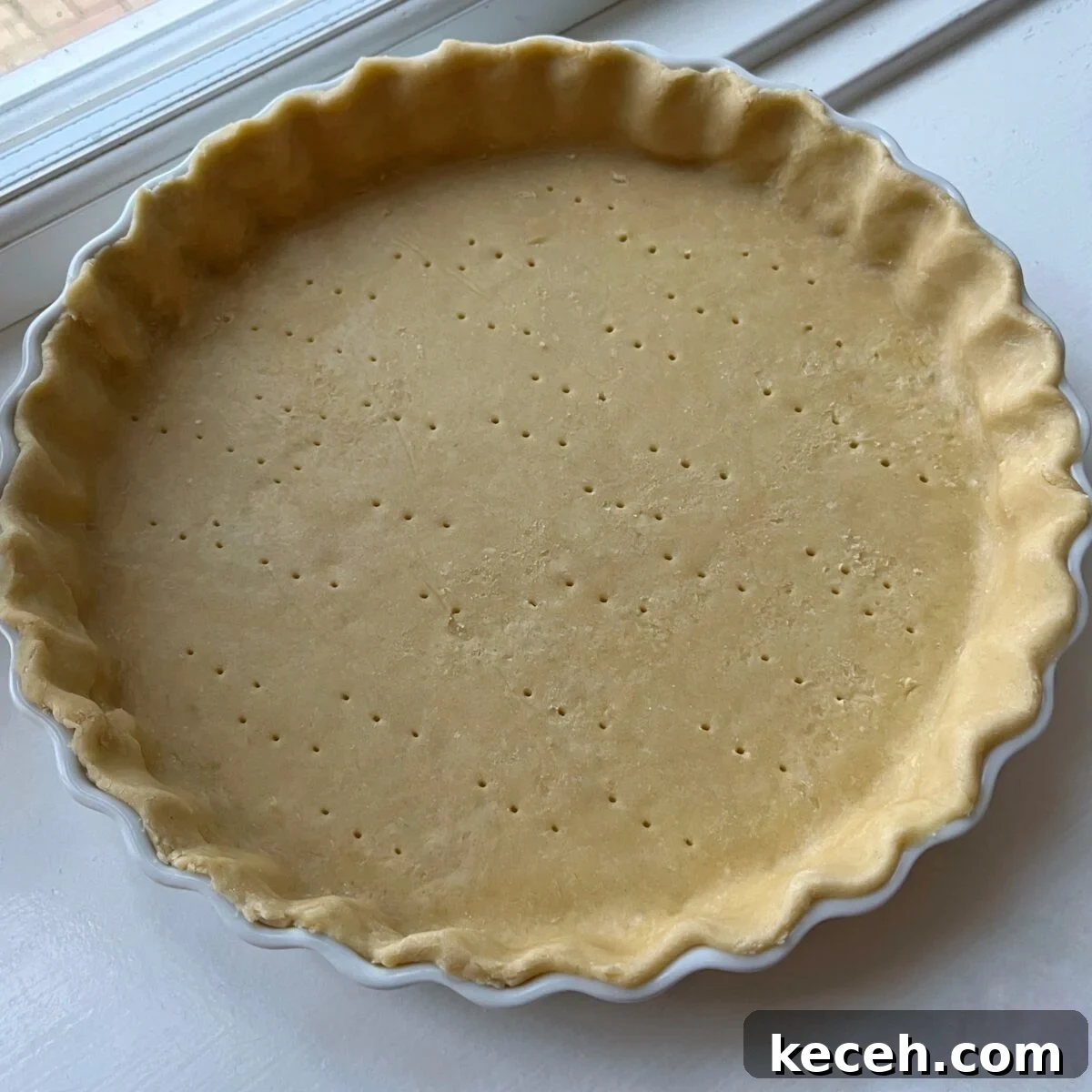 Unbaked pie crust in a fluted ceramic dish with fork holes poked into the base, perfect for a savory chicken quiche.