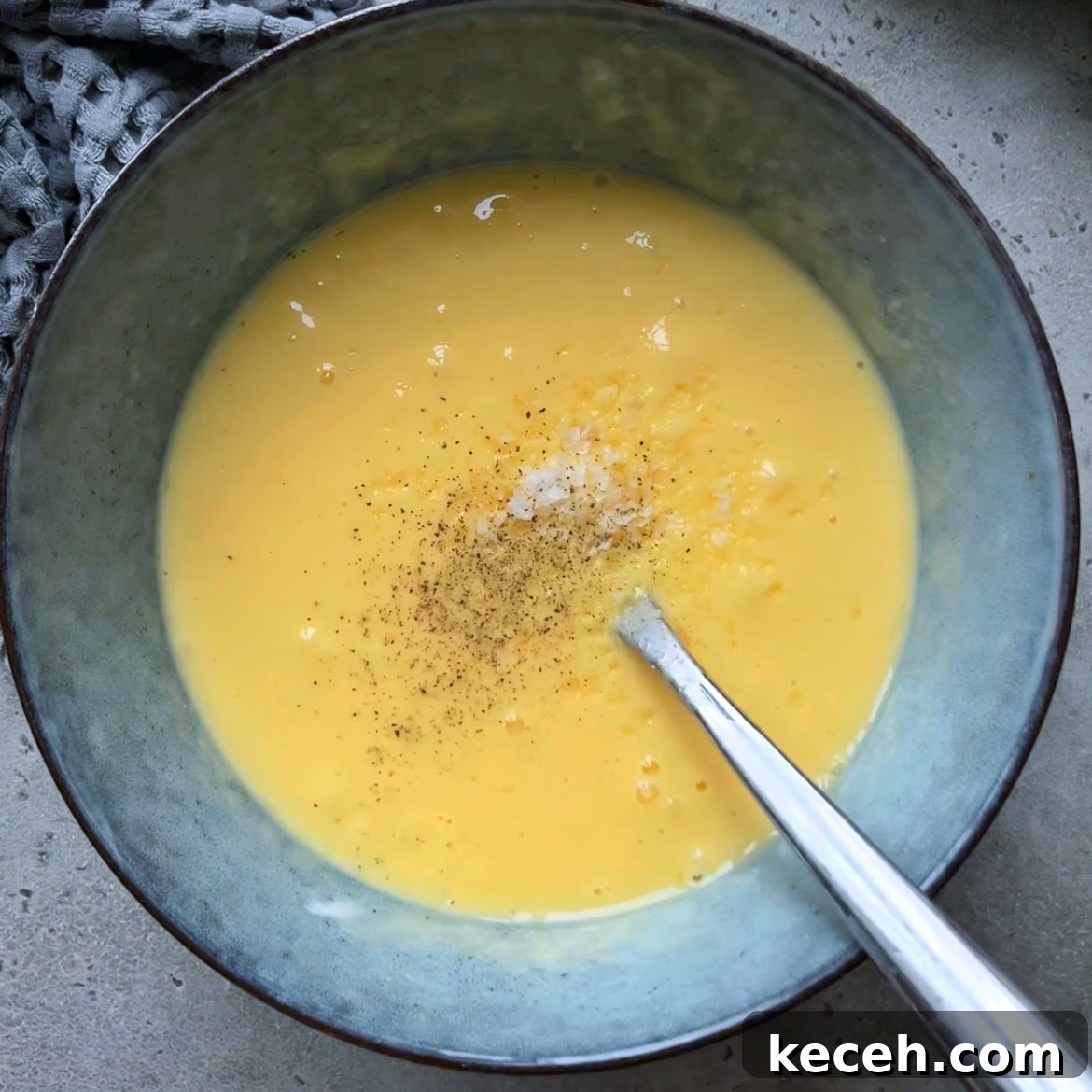 A bowl filled with beaten eggs and sour cream, seasoned with salt and pepper.