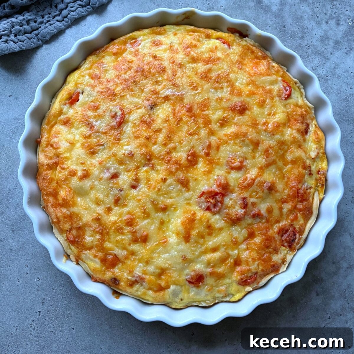 A baked Chicken Quiche with a golden-brown cheese topping in a white fluted ceramic dish.