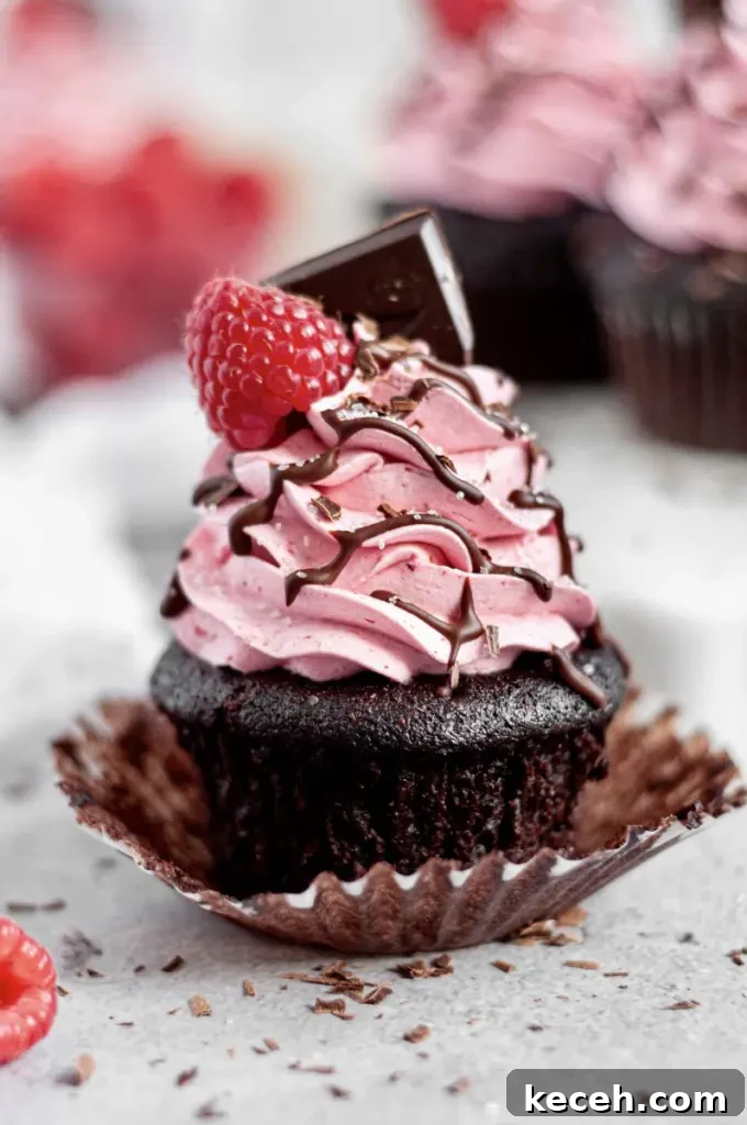 Gluten-Free Chocolate Raspberry Cupcakes with Vegan Option 4 Dark chocolate cupcakes with pink raspberry buttercream swirled on top. There's a bright red raspberry on the top of the frosting swirl with a square of dark chocolate.