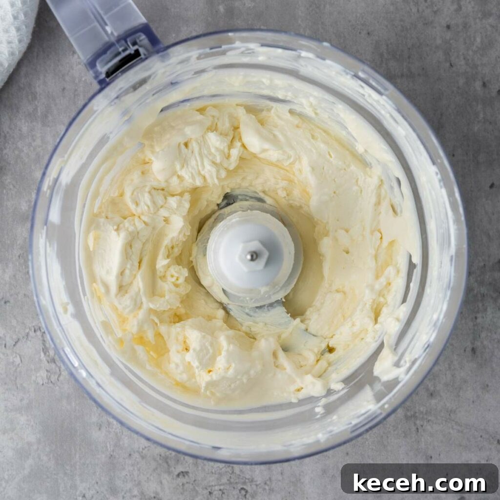 A food processor containing smooth, creamy butter on a gray countertop.