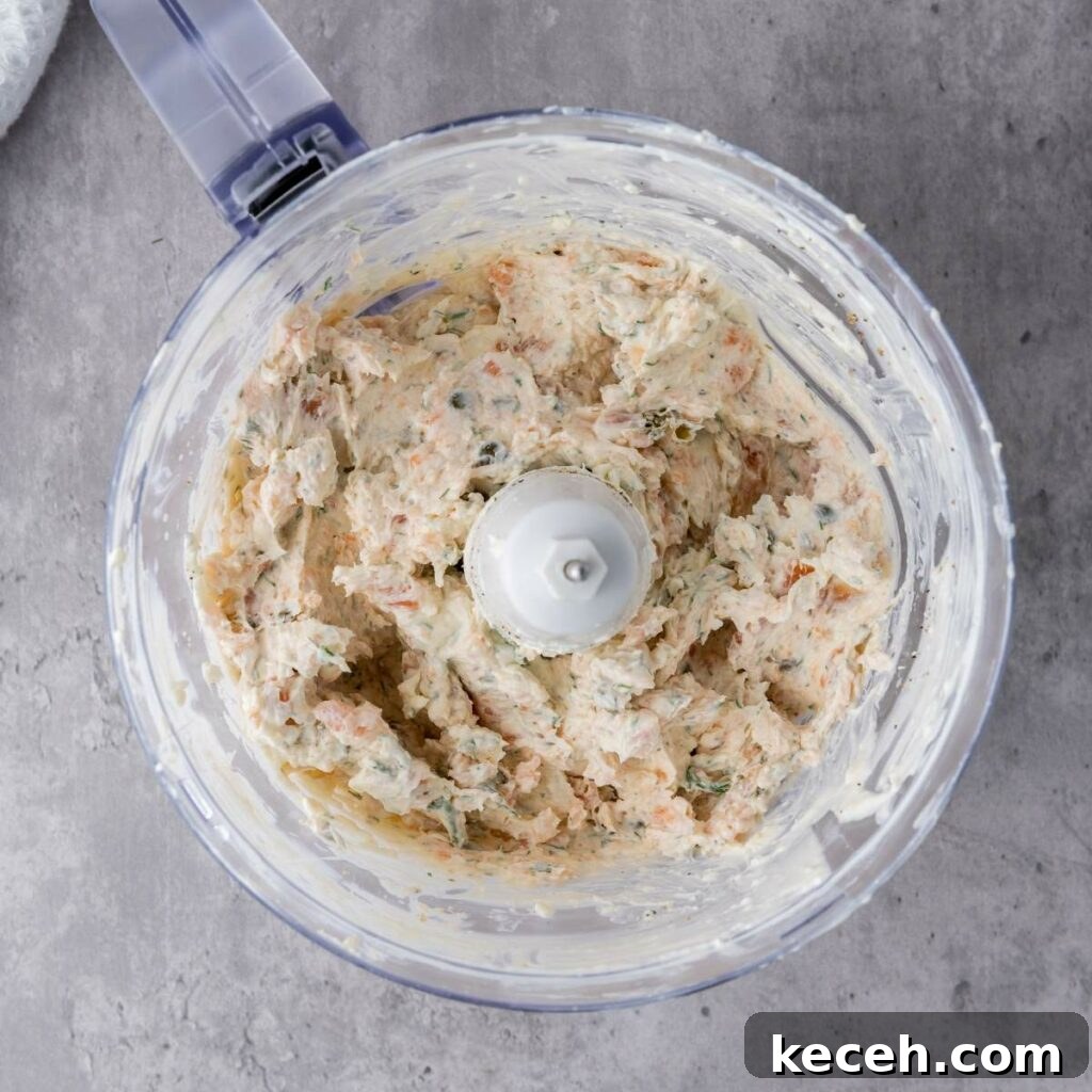 A food processor containing a mixture of chopped ingredients, including herbs, sits on a gray countertop.
