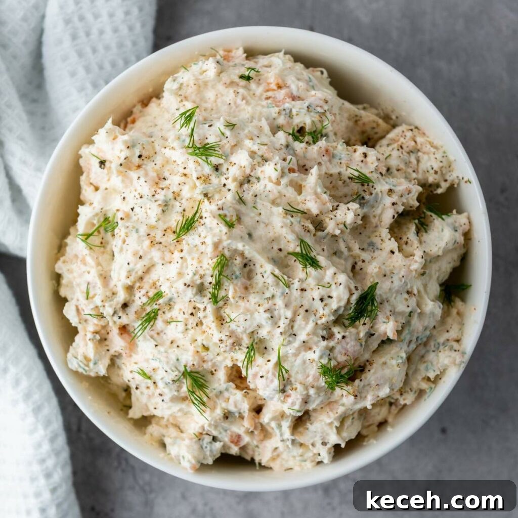 Bowl of creamy dip garnished with dill and black pepper, placed on a gray surface next to a white napkin.