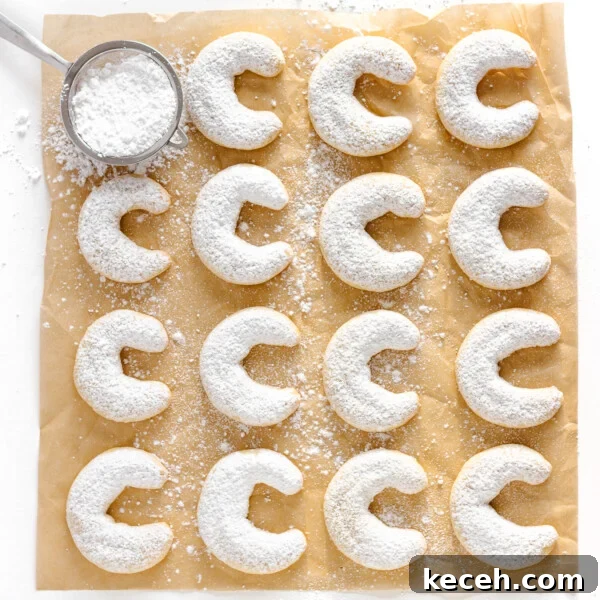 Snowman Chocolate Bark Recipe for Christmas Treats 13 Vanillekipferln (vanilla almond crescent cookies) dusted with powdered sugar and lined up on a square piece of parchment paper.