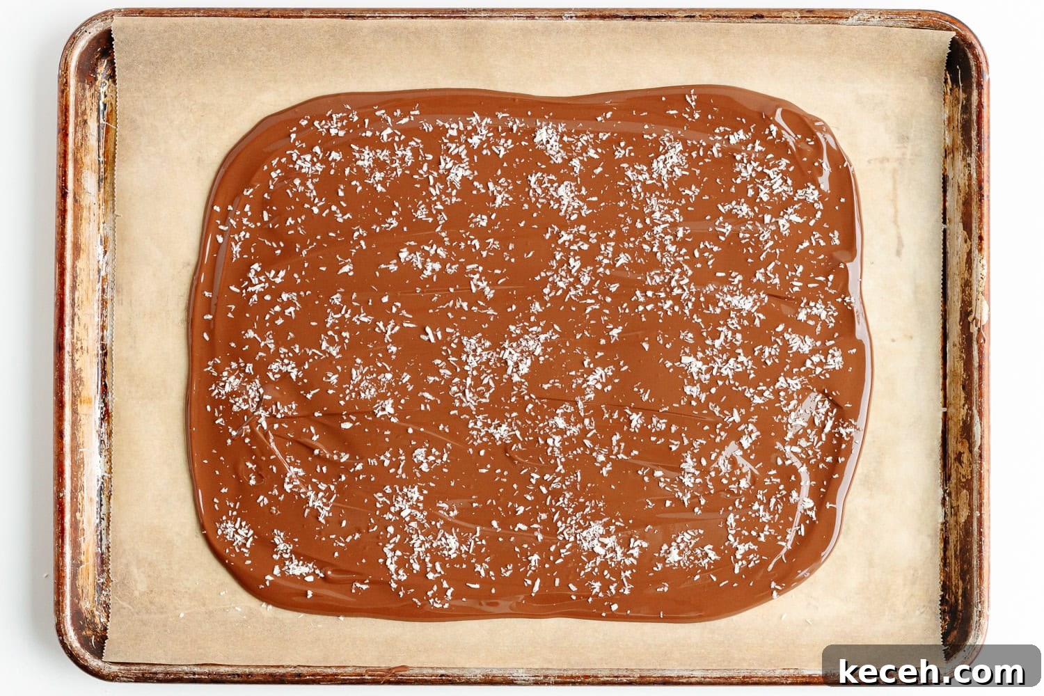 Snowman Chocolate Bark Recipe for Christmas Treats 7 Melted chocolate sprinkled with dried coconut on a parchment lined baking sheet.