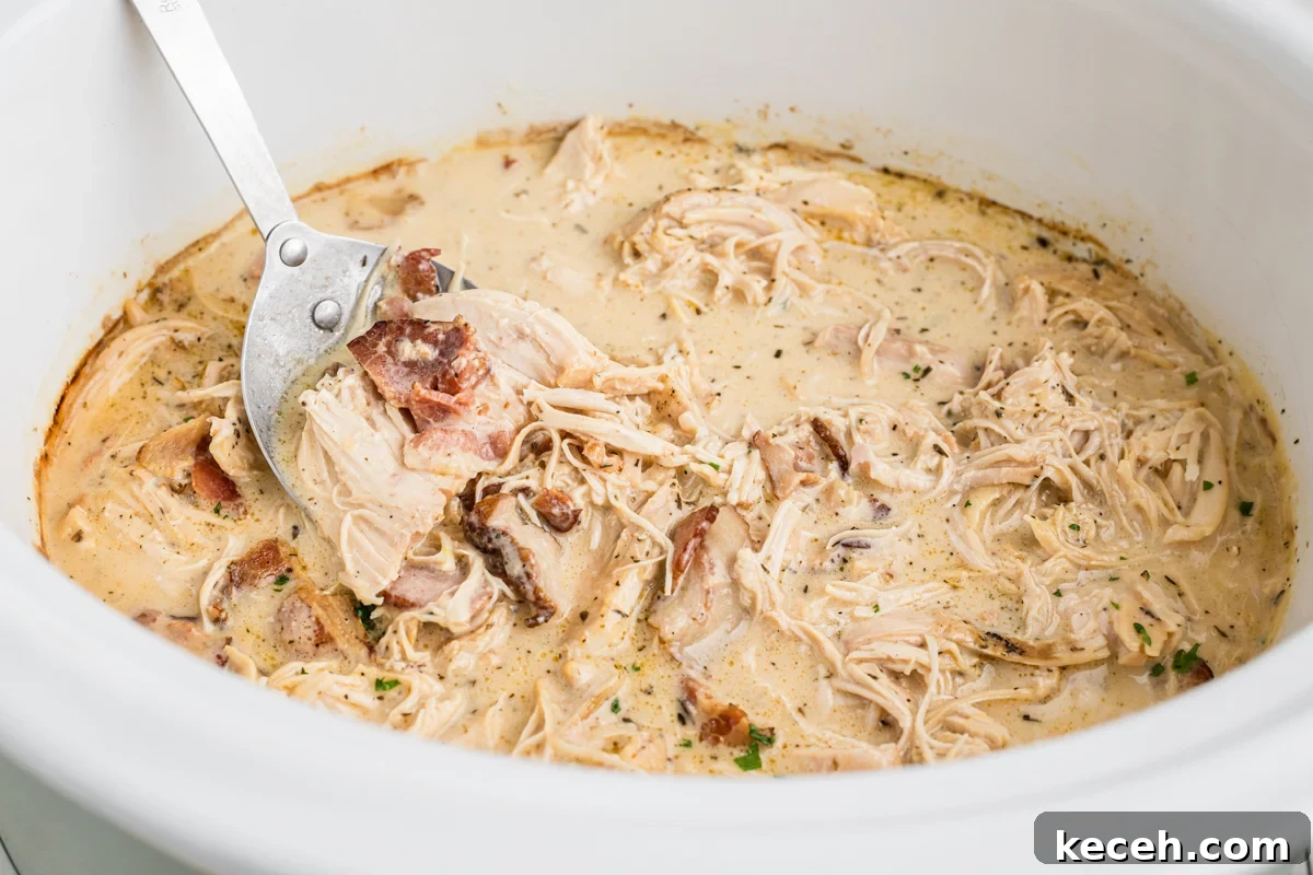 Slow Cooker Chicken in Bacon Gravy — Comforting One-Pot Meal 6 chicken in a creamy bacon gravy with a metal spoon in it.